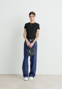 Svart tettsittende t-skjorte, blå vide jeans, svart håndveske med "HUGO" logo, og hvite plattformsko mot en enkel bakgrunn.