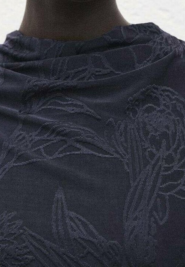 Tissu sombre avec des motifs floraux subtils en relief, drapé autour du cou et des épaules d'une personne, montrant la texture et un design complexe.