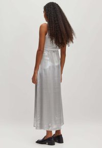Zilveren maxi-jurk met een gladde, glanzende textuur, met een getailleerde taille en een vloeiende silhouet, gecombineerd met zwarte platte schoenen.