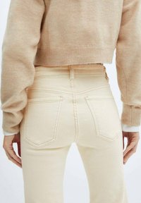 Jeans beige a vita alta con tasche posteriori e cuciture visibili, abbinati a un maglione corto beige chiaro con polsini a costine.