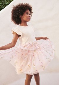 Lichtroze jurk met een uitlopende, gelaagde tule rok met bloemmotieven en pailletten. Top met korte mouwen en ruches.