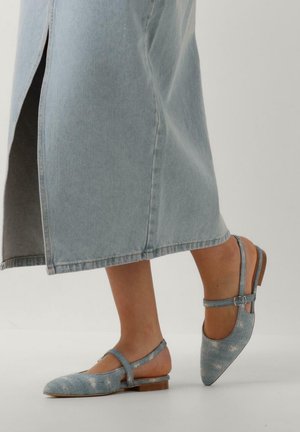 Ben iført falmede blå denimjeans og matchende blå denim spidse flade slingback sko med ankelstropper.