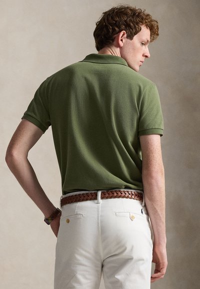 Tummaa vihreä pikeepaita, jossa on teksturoitu kangas, käännetty kaulus ja lyhyet hihat. Yhdistetty valkoisiin housuihin ja punottuun ruskeaan vyöhön.