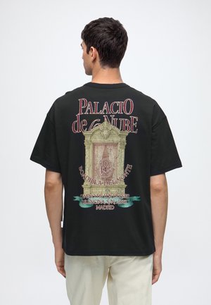 Homme portant un t-shirt noir avec un motif de fenêtre vintage et le texte Palacio de la Nube, Boadilla del Monte, Madrid au dos.