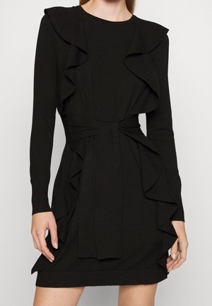 Robe noire à manches longues avec des détails volantés le long des côtés et une ceinture en tissu assortie nouée à la taille.