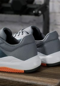 Zapatillas deportivas grises con una parte superior de malla transpirable, suela blanca y un acento naranja en la suela exterior. Presentan un collar acolchado para mayor comodidad.