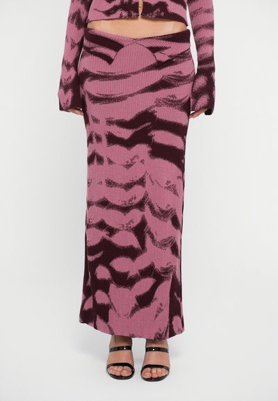 Falda maxi de punto acanalado rosa con patrones abstractos en burdeos oscuro, con un detalle en la cintura y una silueta recta. Combinada con sandalias negras.