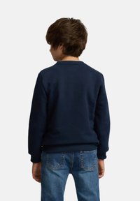 Sudadera azul marino con cuello redondo, puños acanalados, textura suave y cintura ajustada. Lleva puesta un niño con cabello corto castaño.