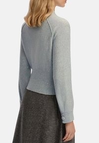 Maglione azzurro chiaro con orlo e polsini a costine, caratterizzato da una superficie testurizzata con piccoli accenti lucidi. Forma definita con maniche lunghe.