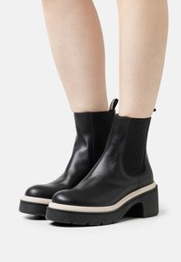 Botas de tobillo de cuero negro con un panel lateral elástico texturizado, suela de plataforma gruesa y una pestaña trasera para facilitar el calzado.