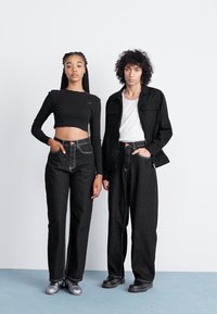 Black cropped long-sleeve top and high-waisted black jeans on a model beside another in a black jacket and white tee, both with textured fabric.