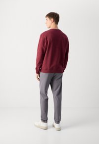 Sudadera marrón con cuello redondo, combinada con pantalones grises de rayas y zapatillas blancas. El conjunto tiene un ajuste relajado y un estilo casual.