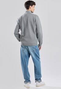 Gray pullover sweater with a high collar, featuring a smooth texture. Paired with loose, light blue denim jeans and white sneakers.