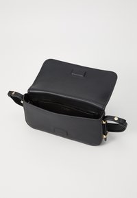 Black leather crossbody bag with a flap and top opening. Features gold hardware and a sleek design. Interior shows a dark lining and brand detail.
