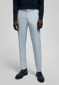 Hellblaue Anzughosen mit geradem Beinschnitt, aus strukturiertem Stoff gefertigt, kombiniert mit schwarzen Leder-Schnürschuhen.