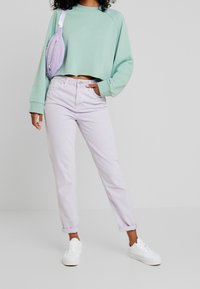 Miętowo-zielony krótki sweter, lawendowe dżinsy, białe trampki i lawendowa nerka. Casualowy strój o luźnym kroju i jasnych kolorach.