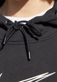 Svart hoodie med dragsnodd och svarta snörändar, ribbad detalj vid halsen och en vit grafisk design över bröstet.