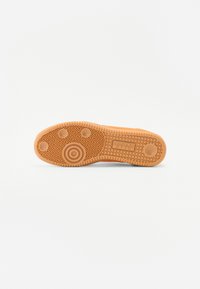 Rubberen sneakerzool in tan met een geometrisch patroon, voorzien van cirkelvormige accenten en verhoogde randen voor grip. Over het algemeen een gladde textuur.