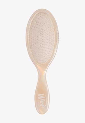 Mokra szczotka o owalnym, przezroczystym korpusie, teksturowanym uchwycie i cienkich szczecinach grzebienia. Kolor to jasny perłowy z logo na uchwycie.