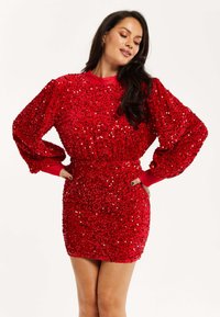 Red sequined dress with long, puffed sleeves and a fitted waist. Smooth texture with shiny sequins creating a bold, reflective surface.