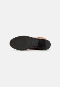 Scarpa in pelle marrone con suola in gomma nera testurizzata. Presenta dettagli cuciti e una finitura liscia nella parte superiore.