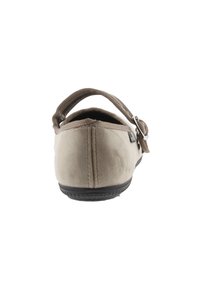 Zapato beige con una textura suave y aterciopelada, parte trasera redondeada y correa elástica. Suela de goma negra con agarre texturizado para estabilidad.