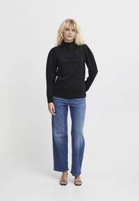 Maglione nero a collo alto con maniche lunghe, abbinato a jeans a gamba larga di un azzurro chiaro, leggermente strappati, e tacchi neri.