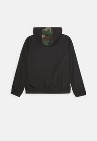 Chaqueta negra con mangas largas y puños elásticos, que cuenta con una capucha con un patrón de camuflaje verde y marrón en la parte trasera.