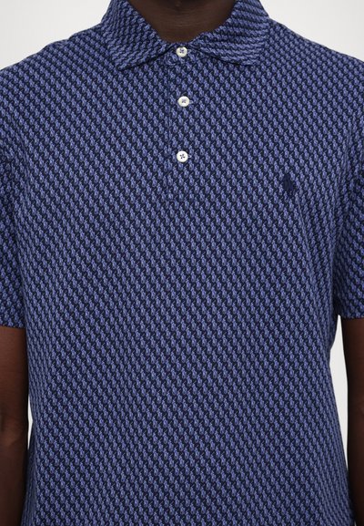 Πόλο μπλο�ύζα σε ναυτική μπλε απόχρωση με επαναλαμβανόμενο ανοιχτό μπλε σχέδιο. Διαθέτει γιακά, τριπλή κουμπότρυπα και κεντημένο λογότυπο στο στήθος.