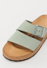 Groene suede slide sandaal met twee brede banden en een metalen gesp, met een kurken voetbed en een getextureerde zwarte rubberen zool.