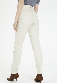 Jeans de tiro alto en beige claro con corte slim, bolsillos traseros y un sutil detalle de costura. Combinados con botas de tacón marrones hasta el tobillo.