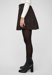 Falda marrón de pana con diseño acampanado, con cintura alta, dos botones delanteros y combinada con medias opacas negras y botas de tacón.