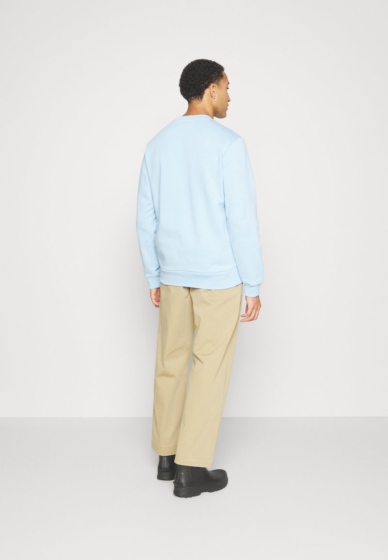 Lichtblauw sweatshirt met een ronde hals, relaxte pasvorm, ribgebreide manchetten en zoom. Combinatie met beige broek en zwarte schoenen.