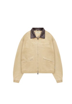 Giacca beige con zip, collo marrone scuro, due tasche laterali diagonali con zip e una tasca orizzontale sul petto, mostrata distesa su sfondo bianco.