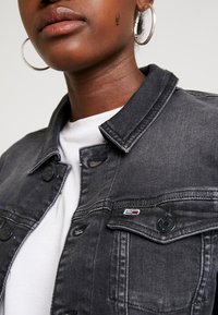 Czarna kurtka dżinsowa z kołnierzykiem, zapięciem na guziki z przodu i dwoma kieszeniami na piersi. Charakteryzuje się subtelnym przeszyciem i małym akcentem logo.