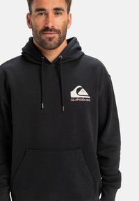 Black hoodie made of soft fabric, featuring a front pouch pocket, drawstrings, and a colorful Quiksilver logo on the left chest.