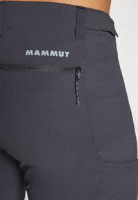 Ciemnoszare spodnie trekkingowe z kieszenią na zamek z tyłu, z logo "Mammut" w odbijającej bieli. Gładki, elastyczny materiał.