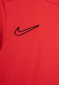 Tela roja con un logo de Nike en forma de gancho bordado en negro en la parte superior izquierda del pecho de una prenda.