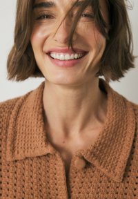 Brown knitted sweater with a textured pattern, collared neckline, and a button detail near the collar. Soft, casual design.