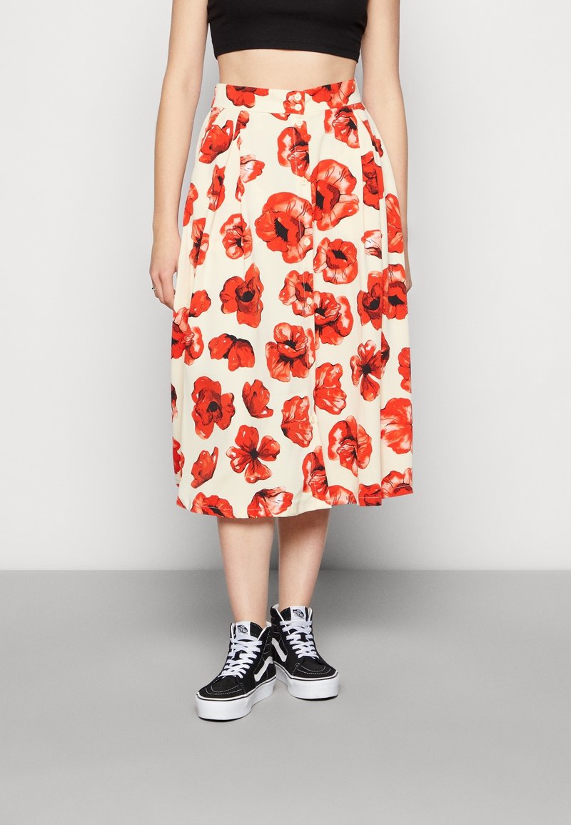 Kukkakuvioinen midi-hame kermanvärisenä, jossa punainen unikon kuvio; siinä on istuva vyötärönauha ja laskokset. Yhdistetty mustiin korkeavartisiin tennareihin.