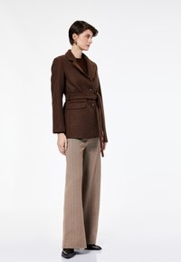 Blazer marrón de mezcla de lana con cintura con cinturón, solapas con muesca, dos botones y bolsillos laterales, combinado con pantalones anchos de rayas beige.