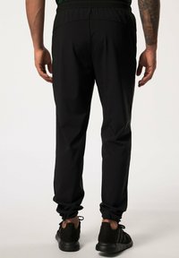 Pantalones deportivos negros con cintura y puños elásticos, hechos de tejido ligero. Presentan una textura suave y un diseño ajustado, ideales para ropa activa.