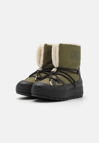 Un paio di stivali invernali verde oliva e neri con suole spesse, lacci neri e rivestimento in pile color crema, marchiati con il logo Tommy Hilfiger.