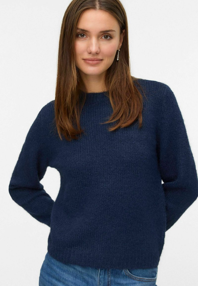 Námorně modrý texturovaný svetr s kulatým výstřihem a dlouhými rukávy, doplněný o modré džíny, který ukazuje neformální design.