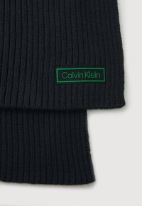 Zwarte geribde gebreide sjaal met een groene rechthoekige label met de tekst "Calvin Klein" in een vet lettertype. Zachte textuur, warme en veelzijdige design.