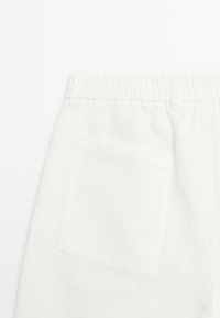 Pantalon en lin blanc avec une taille élastique, une poche au dos et une coupe droite avec une texture lisse et légère.