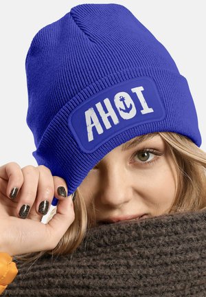 Blue knitted beanie featuring a white patch with "AHOI" and anchor design. Textured fabric with a snug fit, rolled hem for style.
