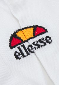 Weißer Stoff mit einem gestickten Logo in Rot, Gelb und Schwarz, das eine kreisförmige Form und kräftige Buchstaben zeigt.