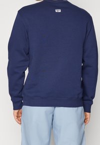 Mörkblå sweatshirt i mjukt tyg, med rund halsringning, ribbade ärmslut och nederkant, samt en liten logotagg på baksidan.