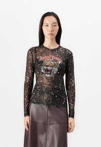 Must mustalönguse särgiga, millel on läbipaistev materjal, loomade print ja värviline tiigerigraafika. Tekst "Joop! Jeans" punases värvitoonis graafika kohal.